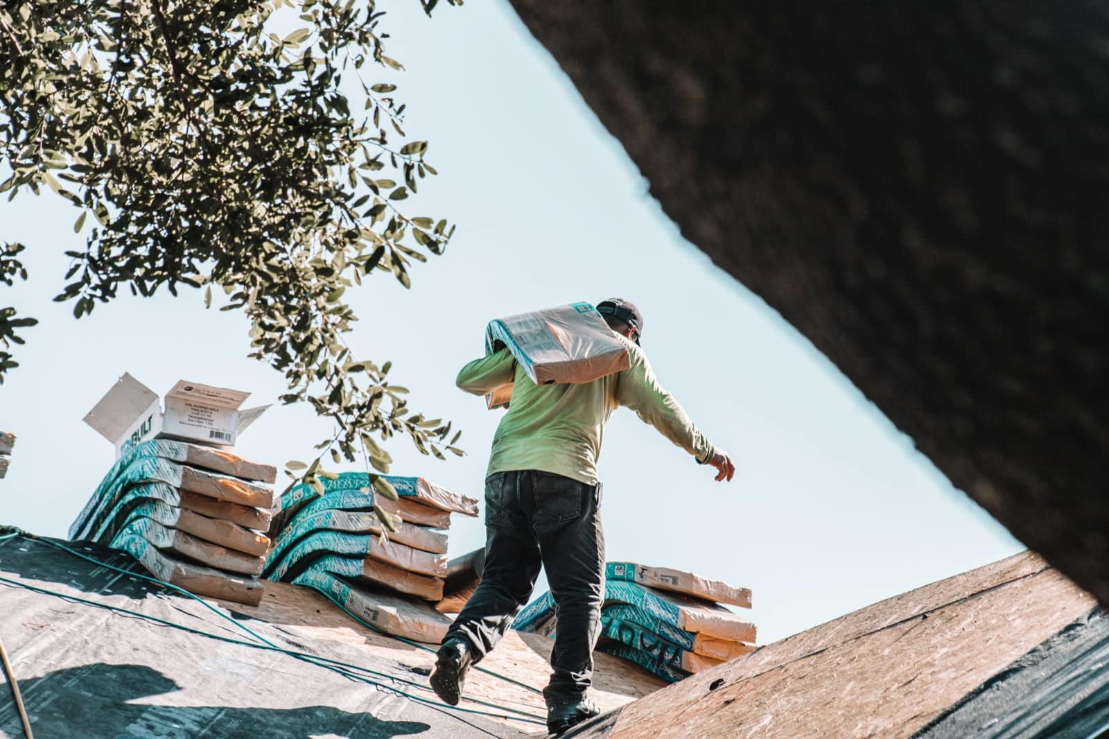 Roofer on a residential pitched roof tearing off asphalt shingles in late afternoon light